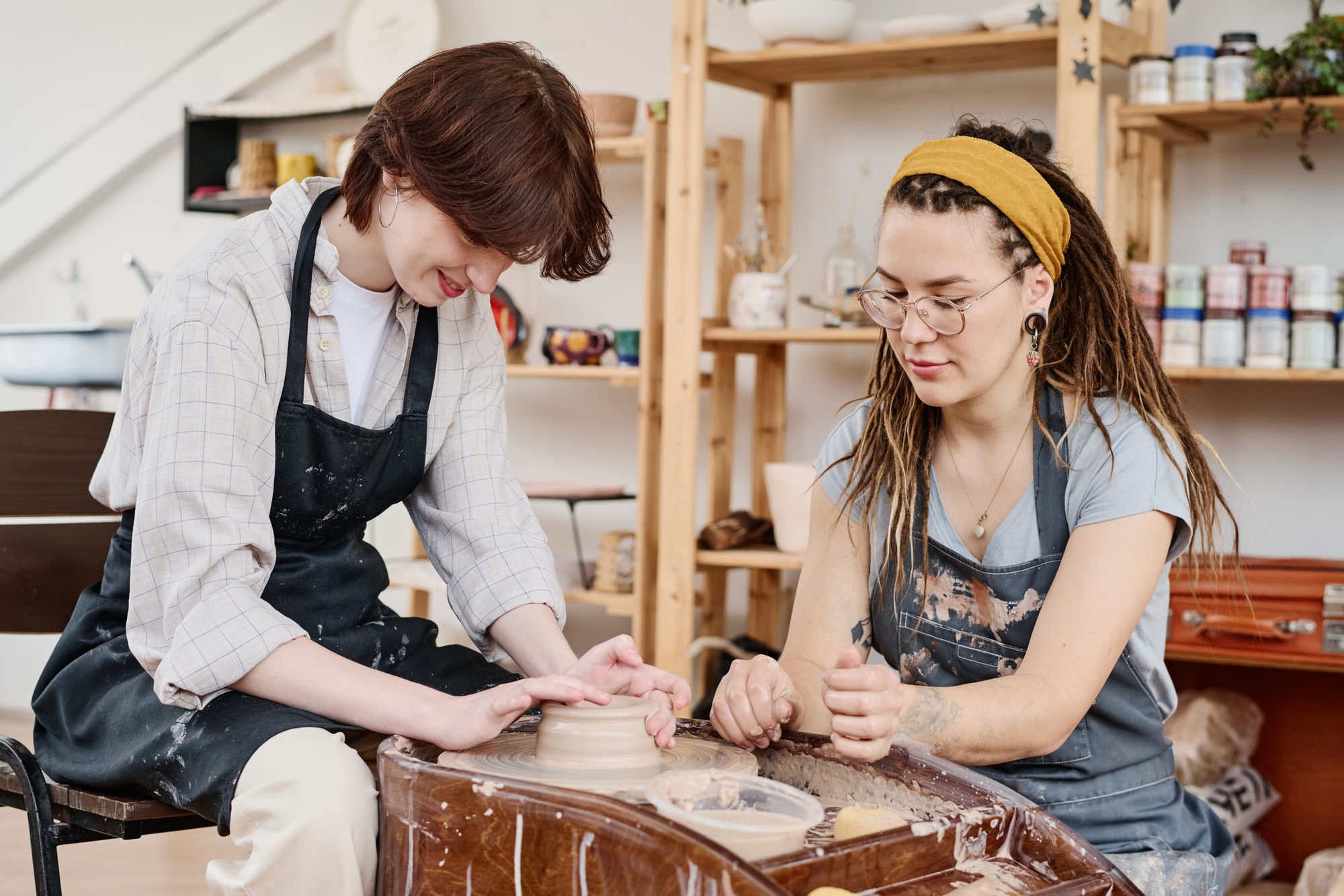 young-female-master-of-pottery-consulting-girl-in-workwear-sitting-by-wheel.jpg